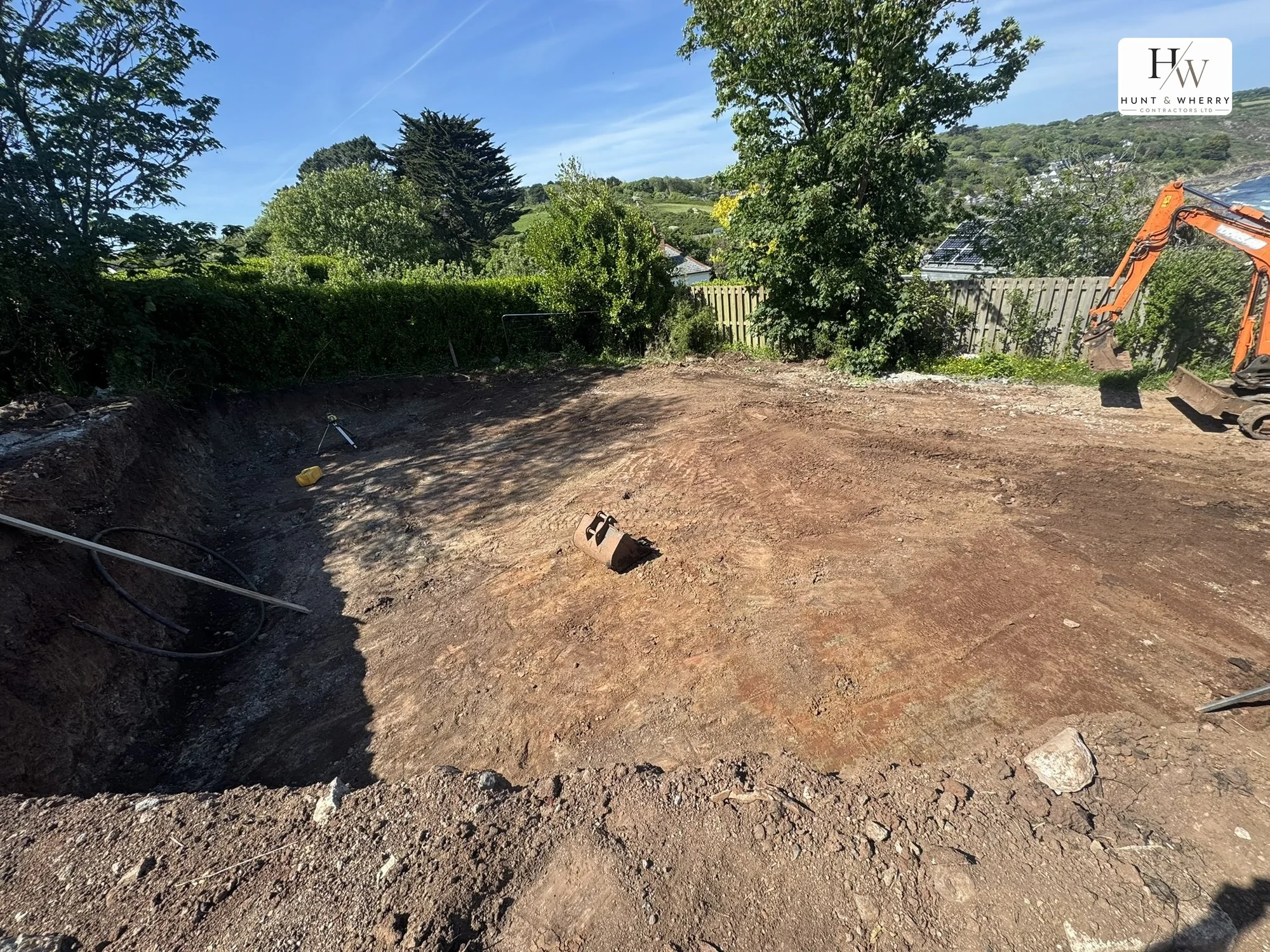 Building plot excavated and levelled above a Cornish coastal village, with the sea beyond