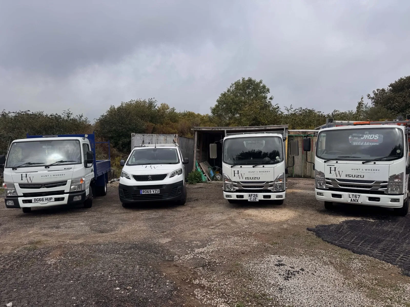 The HW Contractors fleet parked front-on in the yard: a Mitsubishi tipper, the Peugeot van and two Isuzu tippers, all in Hunt & Wherry livery