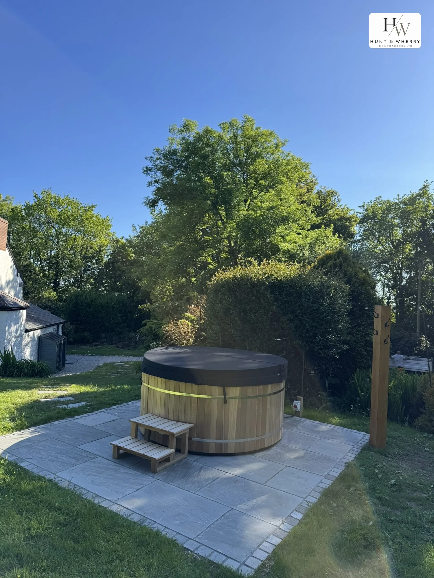Hot tub seated on a riven paved base with a granite sett border, set into the lawn of a Cornish cottage garden