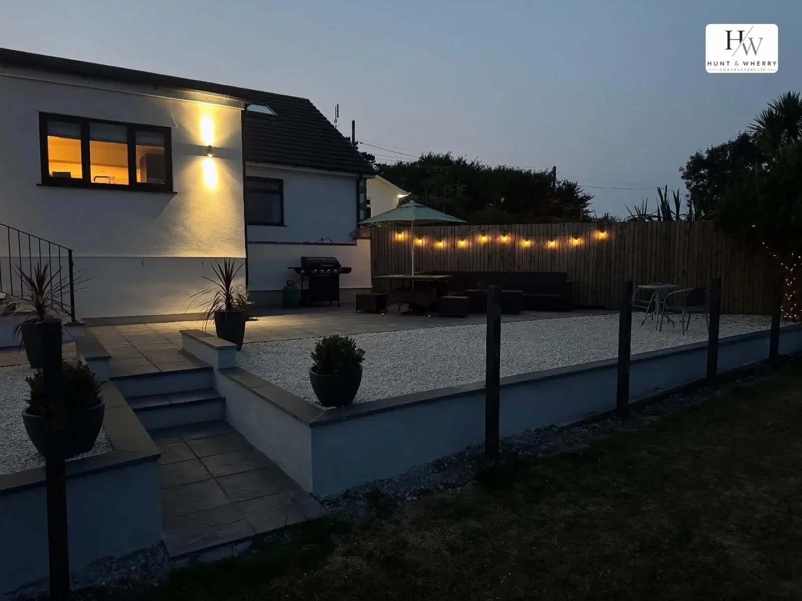House and raised patio at dusk with garden lighting