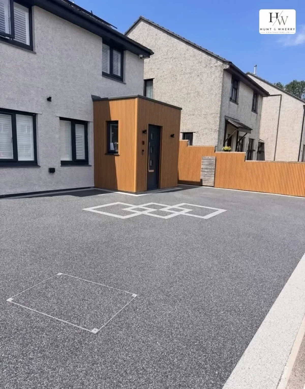 Grey resin bound driveway with a white inlaid pattern outside a modern home