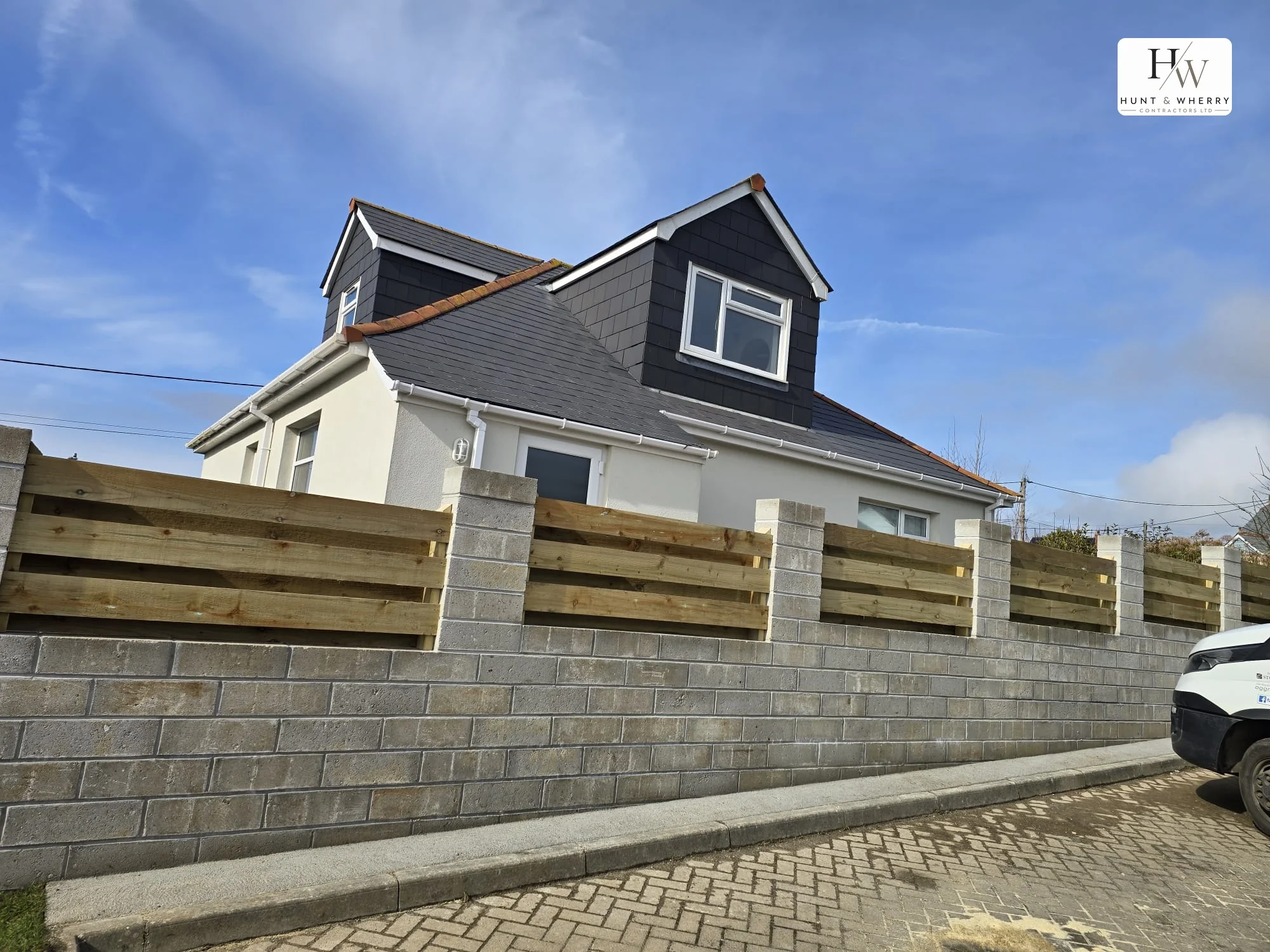 Concrete blockwork retaining wall with piers and timber sleeper fencing above, alongside a new kerb line and block paved apron