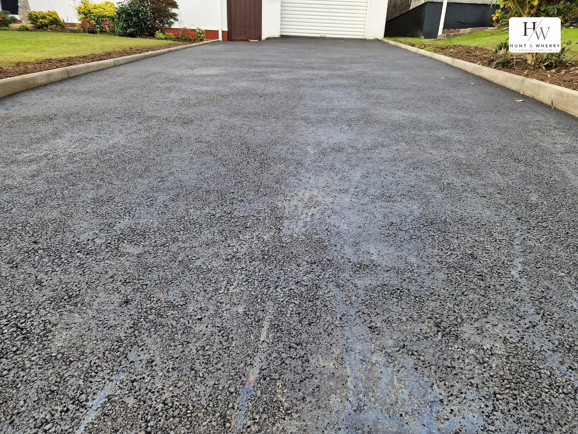 Close view of a freshly laid tarmac driveway surface between new concrete kerbs