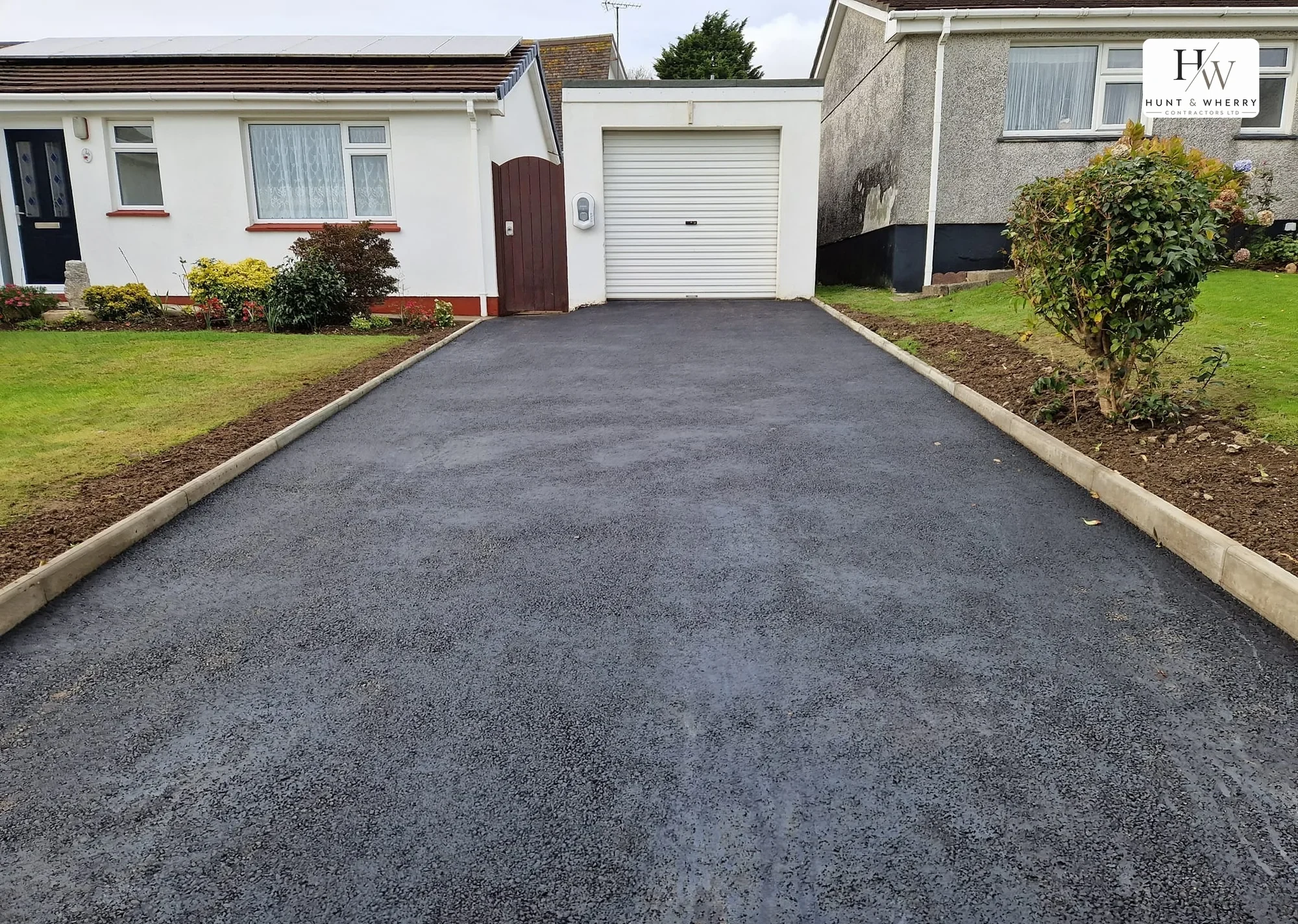 Newly laid tarmac driveway with concrete kerb edging running up to the garage of a Cornish bungalow