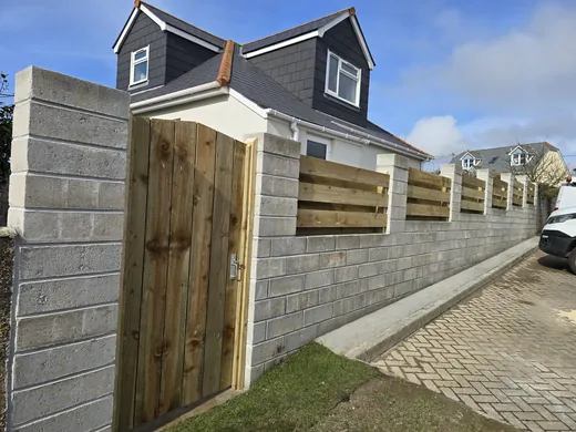 Concrete block retaining wall with a timber fence and gate above a block paved drive