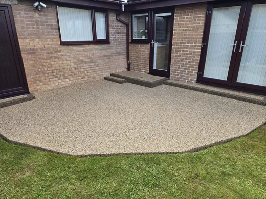Buff resin bound patio curving around a red brick bungalow