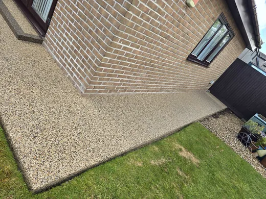 Golden resin bound driveway meeting the lawn beside a brick house