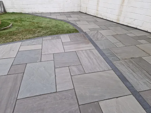 Grey sandstone path with a charcoal border running beside a lawn