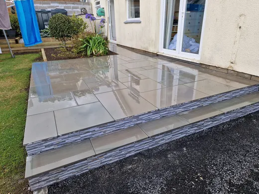Grey porcelain patio with a slate edging course beside a cream house